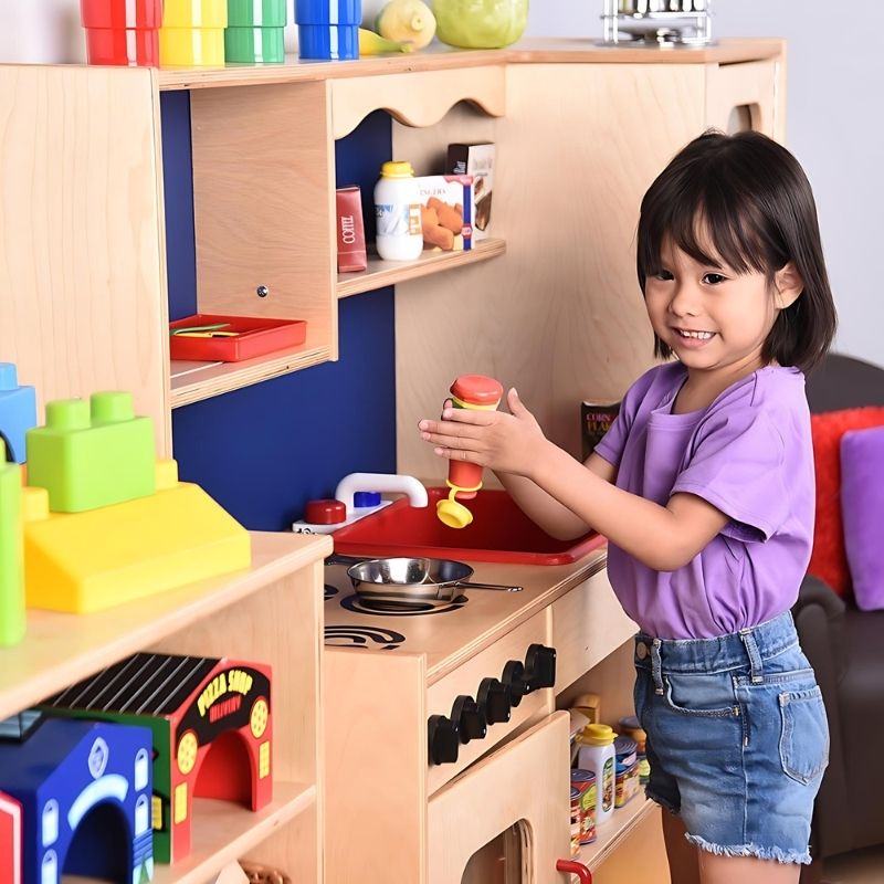Close-up view of a child playing at the Constructive Playthings Five-In-One Kitchen, showing the turning stove knobs and acrylic oven panel detail on this classroom play kitchen