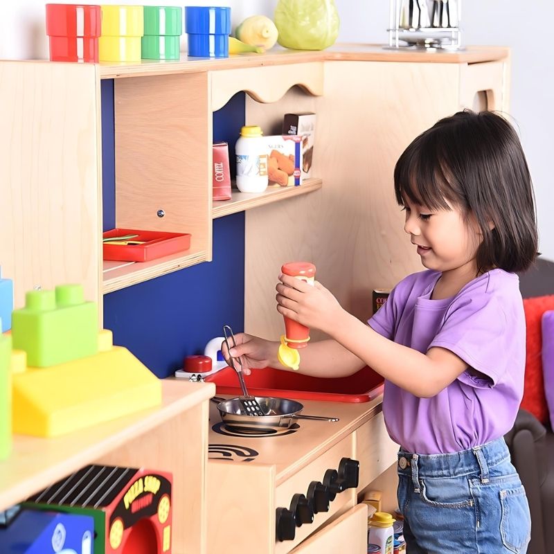 Child engaged in pretend cooking at the Constructive Playthings Five-In-One Kitchen, demonstrating the realistic acrylic oven and microwave panels and turning knobs