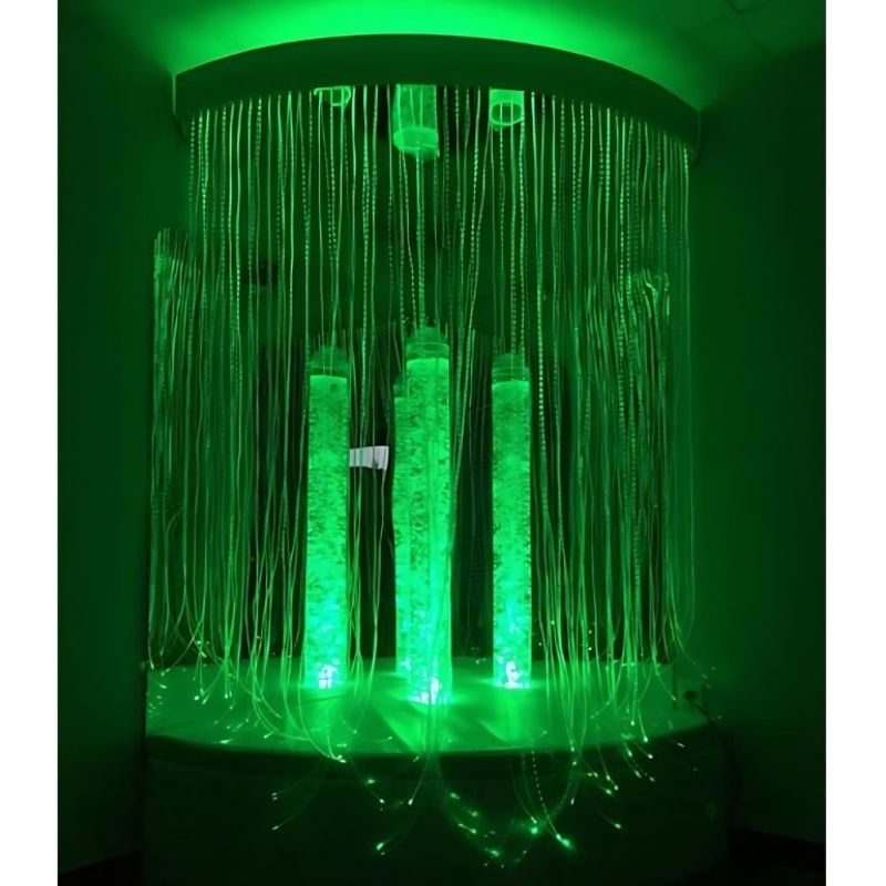 Experia Calming Sensory Cocoon landscape view in green light showing the bubble tube, Calming Corner Shower fibre optic curtain, and ceiling mirrors creating an immersive enclosed sensory environment