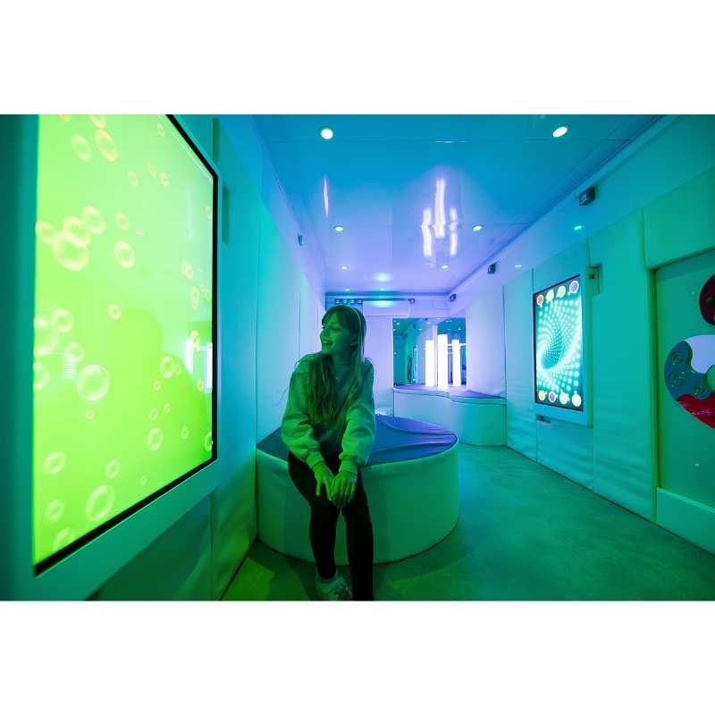 Teen seated and engaging with the Experia Intelli Panel Bubble Wall interactive sensory panel in a green-lit room