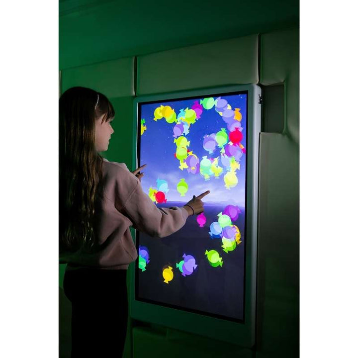 Side view of a child engaging with the Experia Intelli Panel Particle sensory wall panel in a green-lit therapy room