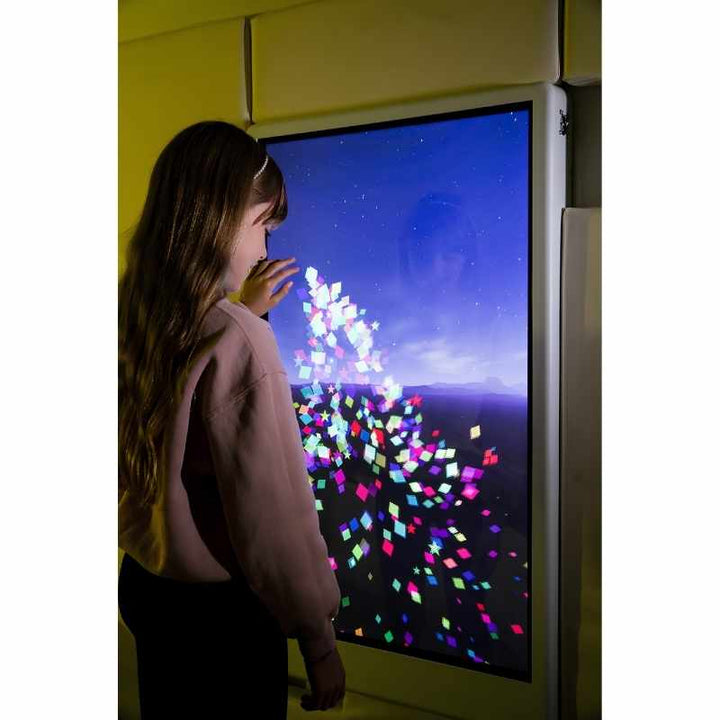 Rear view of a child engaging with the Experia Intelli Panel Particle touchscreen sensory wall panel in a yellow-lit room