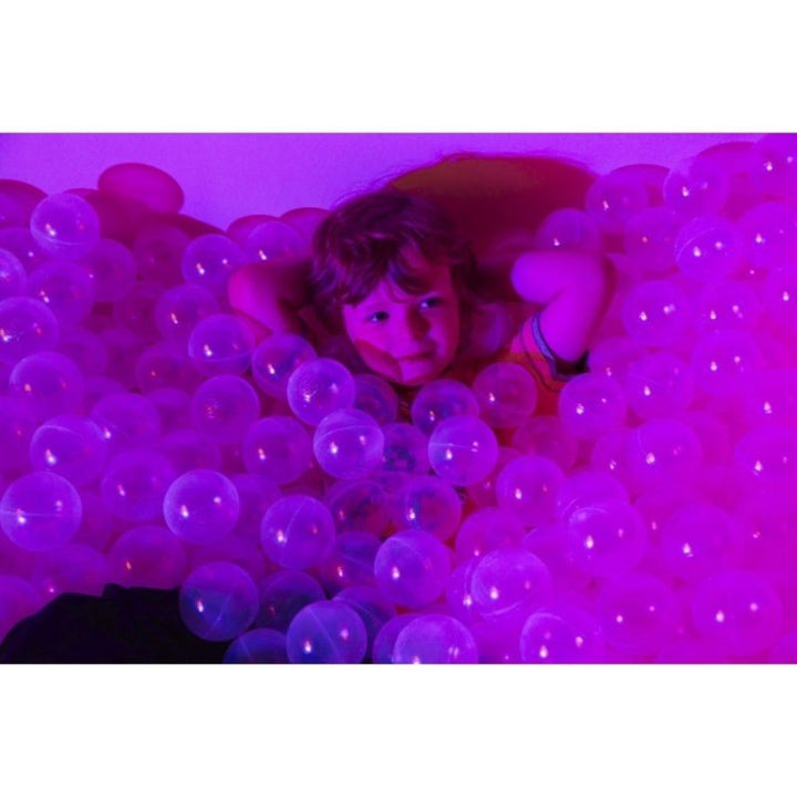 Child playing in the Experia Interactive LED Ball Pool in pink light, showing the immersive full-pool colour change and the sensory ball pool experience for children