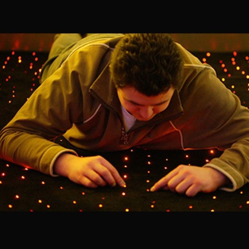 Adult crawling on the Experia LED Fibre Optic Star Carpet demonstrating the full-size 2m x 1m floor coverage and handmade colour-changing fibre optic star-field effect