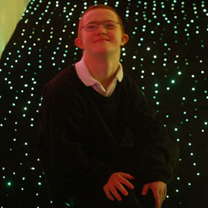 Child smiling while lying on the Experia LED Fibre Optic Star Carpet, showing the joy of close floor-level contact with the colour-changing fibre optic lights in the black carpet surface