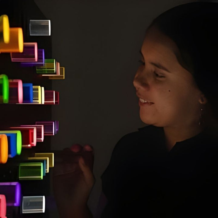 Adult using the Experia PixelPop Interactive Light Panel in a darkened room, showing the brilliant glowing effect of the coloured pegs against the black background