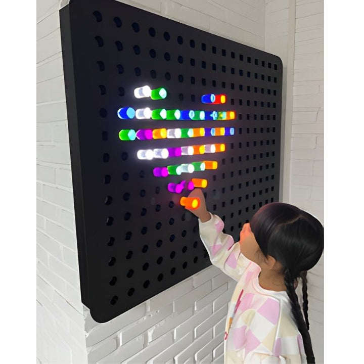 Child interacting with the Experia PixelPop Interactive Light Panel, inserting glowing coloured pegs into the giant 40"x32" LED sensory peg board