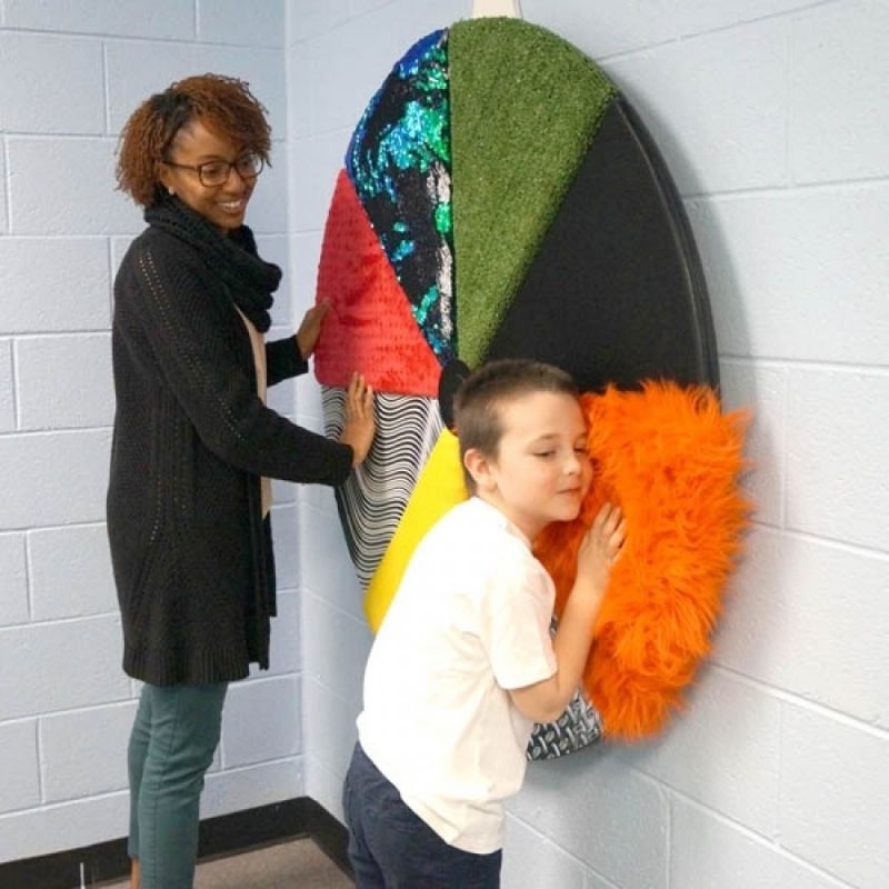 Adult and child exploring the Experia Sensory Texture Wheel together, touching the tactile texture panels on the 46" wall-mounted sensory activity wheel