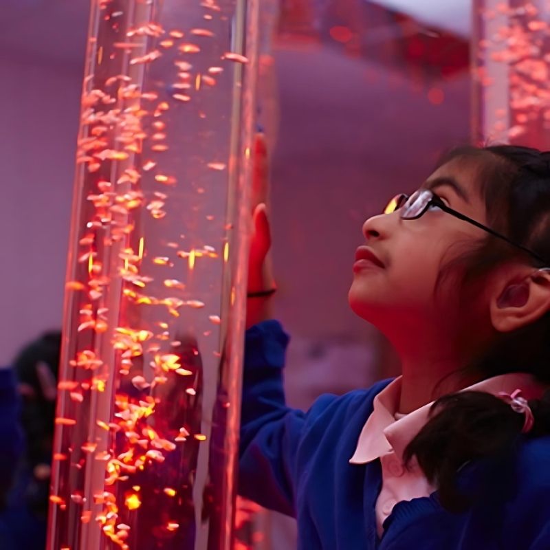 Child actively pressing the base colour buttons on the Experia Touch Sensitive LED Sensory Bubble Tube, demonstrating the minimal-pressure cause-and-effect colour change