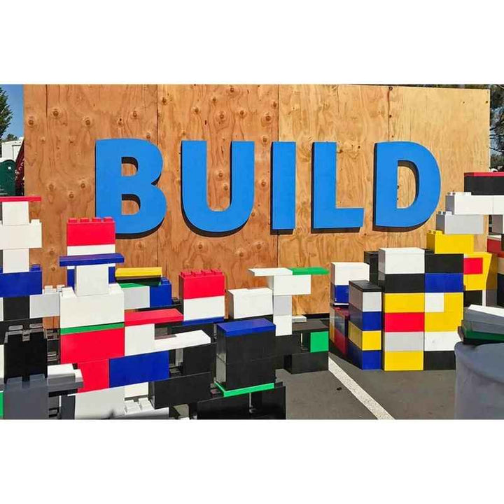 Children's structures built from EverBlock giant building blocks beneath a BUILD sign, showing outdoor STEM building play