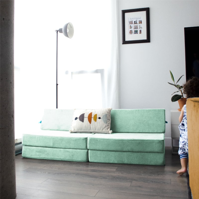 Child actively playing on the Go Coconut Half Coconut modular foam couch, demonstrating climbing and vestibular sensory development
