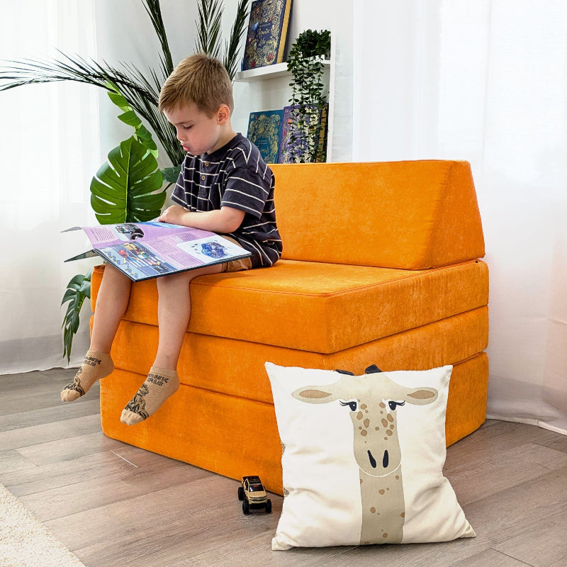 Child reading a book while seated on the Go Coconut Half-Coconut Maxi Bundle modular play couch in orange, showing the compact kids' foam couch in couch configuration