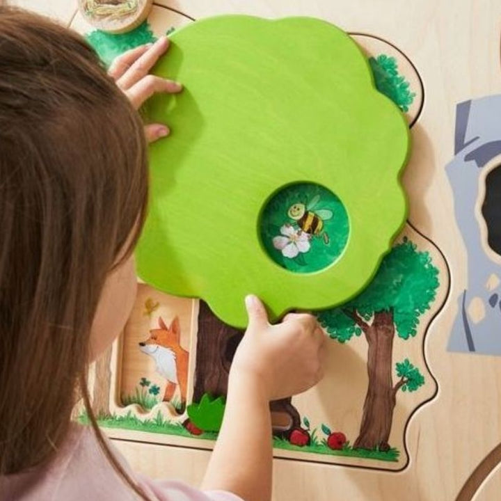Close-up of a child's hands interacting with the HABA Pro Forest Sensory Wall Panel, demonstrating fine motor engagement with the sliding elements