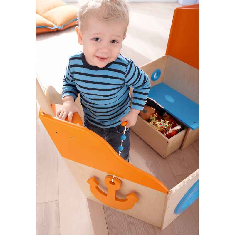 Toddler reaching for the hanging anchor pull toy on the HABA Play Sailboat, a wooden playhouse built for cooperative play