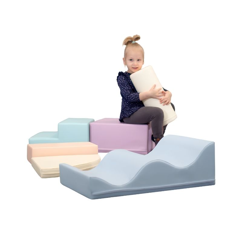 Toddler girl hugging a foam cylinder while sitting on the IGLU Explorer Soft Play Set in a pastel colourway