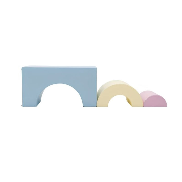 The three individual foam pieces of the IGLU Rainbow Bridge Soft Play Set laid out separately - large blue bridge arch, medium cream arch, and small pink half-dome - showing each shape