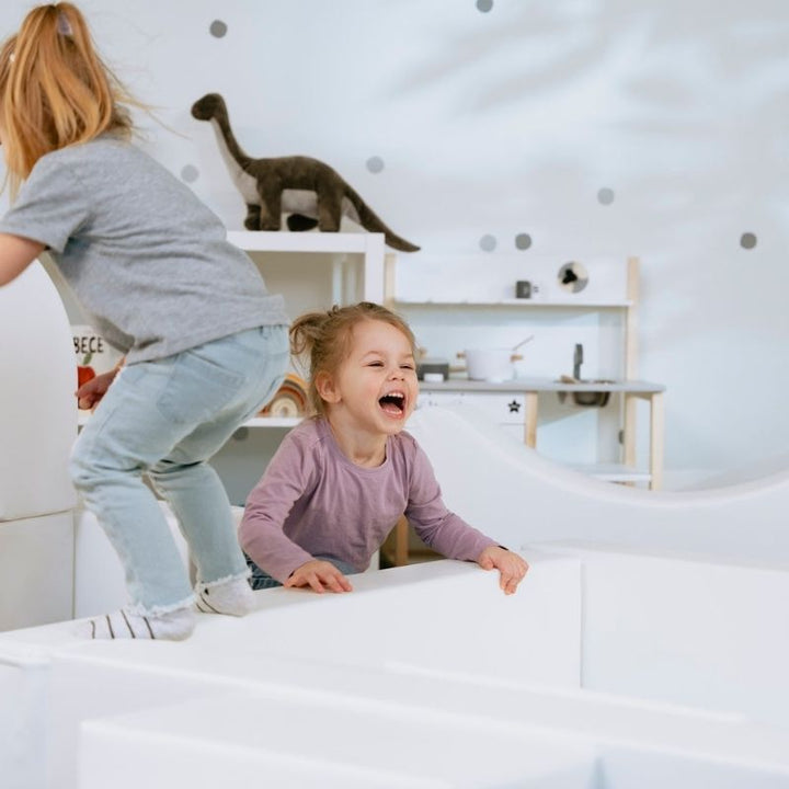 Two girls playing on the IGLU Soft Play Party Set, showing the foam step and slide configuration in a home or daycare setting