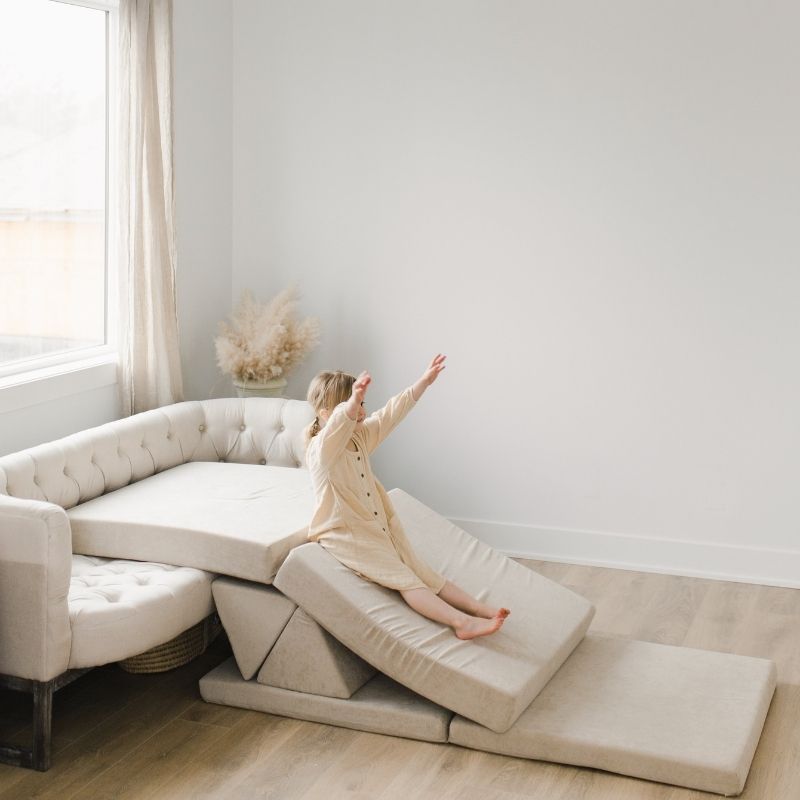 Child sliding on the Kiddie Couch modular play couch in Sand Beige, supporting vestibular input and active gross motor play