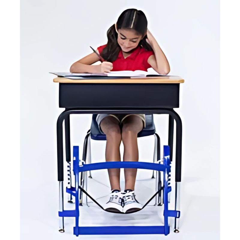 Child using the Kinnebar K100 Foot Swing in blue while studying at a school desk, showing how the under-desk foot swing supports focus during seated tasks