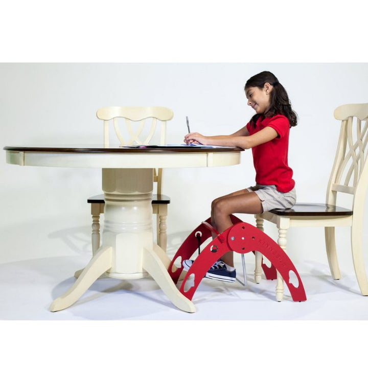Side view of a girl using the Kinnebar K200 Foot Swing at a desk while studying, showing in-seat movement and sensory input during a learning task