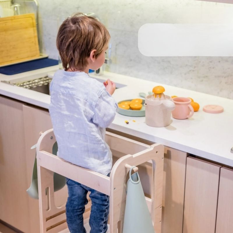 Child actively engaged at the Sapiens Child Kiwi Kitchen Tower, demonstrating the purposeful fine motor activity and independent participation the adjustable learning stool supports