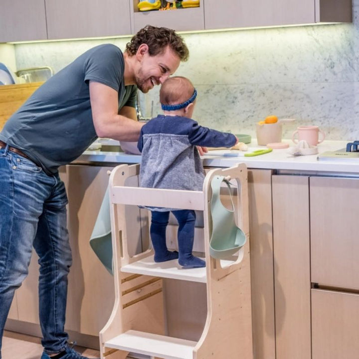 Father and child using the Sapiens Child Kiwi Kitchen Tower together at counter height, showing the adjustable learning stool supporting toddler kitchen participation and family cooking