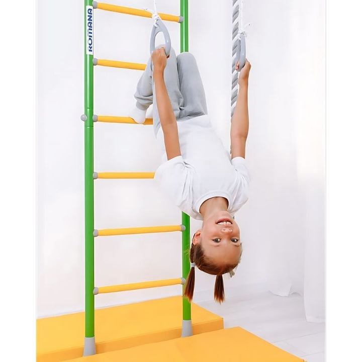 Child hanging upside down on the LimiKids Comet indoor playset, showing the gymnastic rings and trapeze in use for vestibular stimulation, core strength, and body awareness development