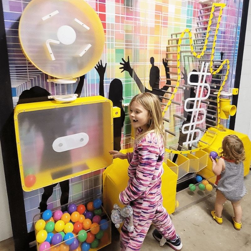 Two children playing with the LiteZilla Ultimate Ball Launcher sensory exhibit, interacting with the colourful ball collection tray and air-powered launch mechanism at a children's discovery space