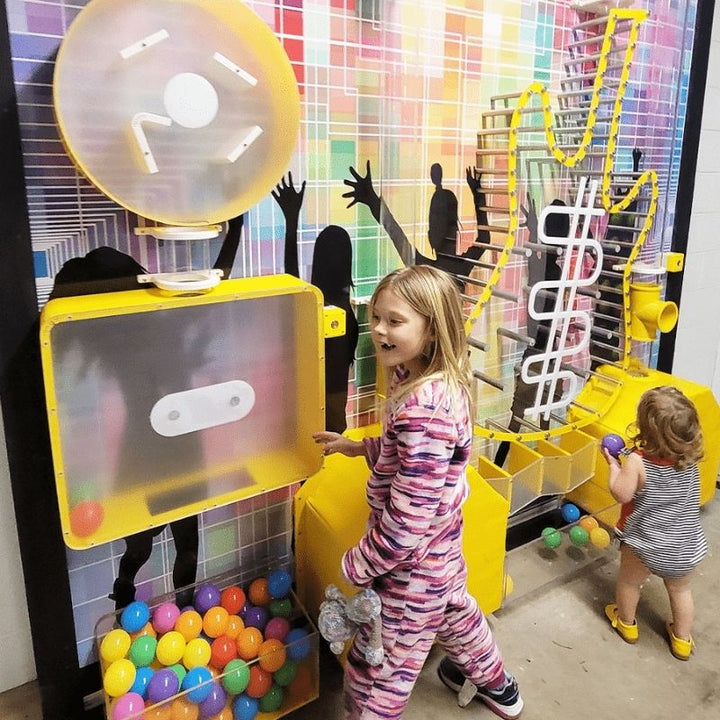 Two children playing with the LiteZilla Ultimate Ball Launcher sensory exhibit, interacting with the colourful ball collection tray and air-powered launch mechanism at a children's discovery space