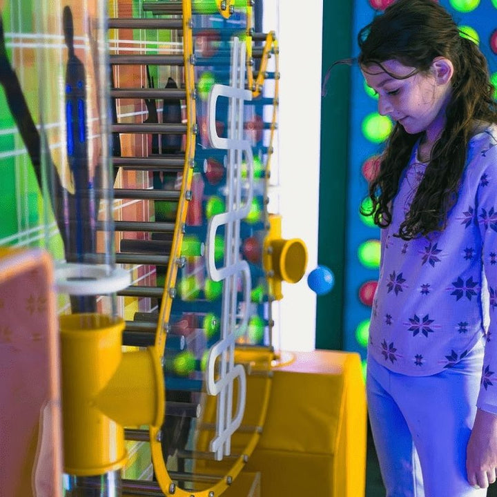 A child watching balls travel through the chain conveyor pathway of the LiteZilla Ultimate Ball Launcher, capturing the focused cause-and-effect engagement the STEM sensory exhibit delivers