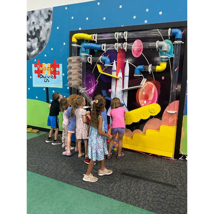 A group of young children gathered together at the LiteZilla Ultimate Ball Launcher in an indoor play centre, showing how the air-powered STEM sensory exhibit naturally draws groups into shared interactive play