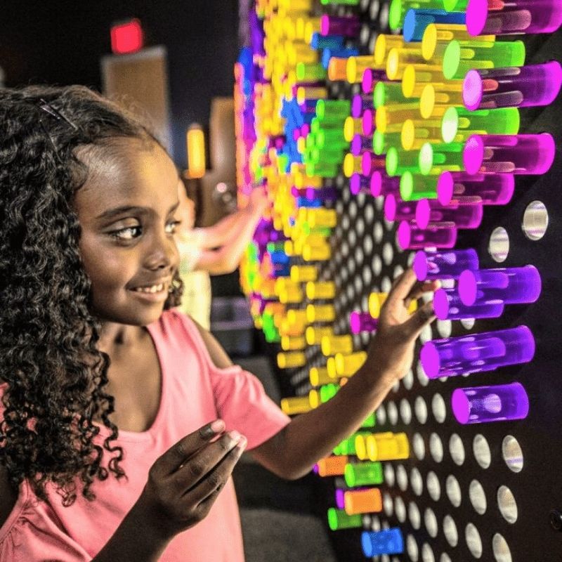 Close-up side view of a girl placing LitePins into the LiteZilla Giant Lite Brite, showing tactile engagement and fine motor precision