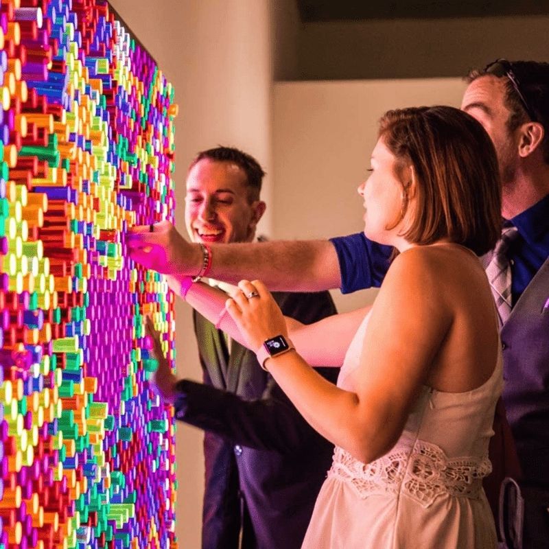 Three adults collaborating on a LiteZilla Giant Lite Brite interactive sensory light wall, creating a glowing design with colourful LitePins