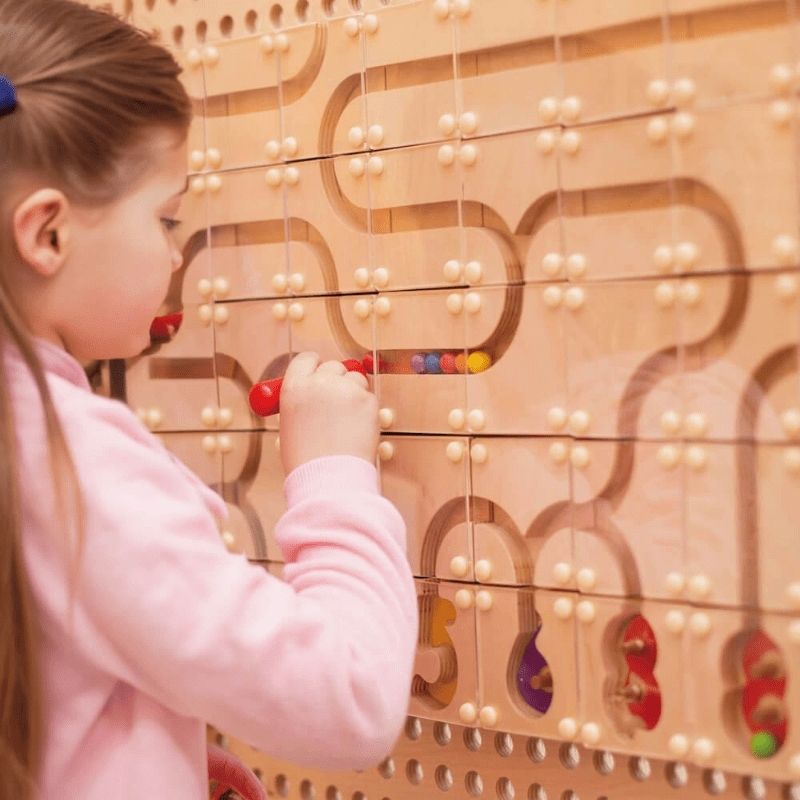 Child threading colourful beads through a curved bead maze panel on the LiteZilla KidWorx wall-mounted learning system, supporting fine motor development and cognitive sequencing