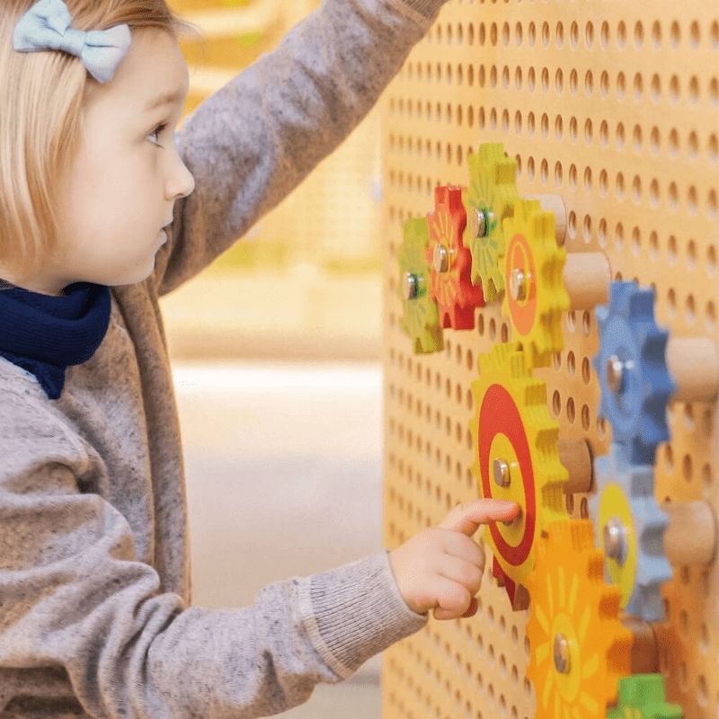Child pressing colourful spinning gears on the LiteZilla KidWorx Interactive Design Suite beechwood wall grid, a hands-on STEM learning system for classrooms and therapy spaces