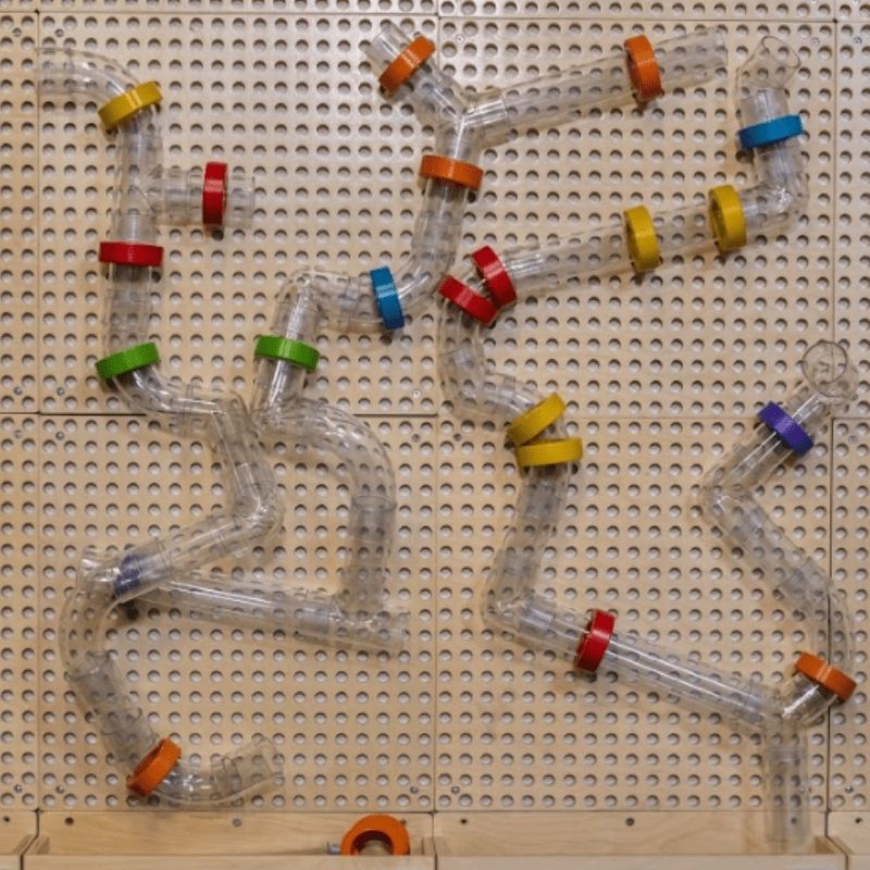 Close-up of the LiteZilla KidWorx Tube Maze activity showing transparent tubes and colourful connectors assembled on the beechwood grid, a hands-on STEM construction activity for tactile and spatial learning