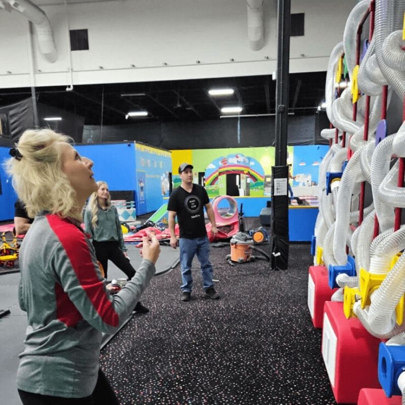 Adults interacting with the LiteZilla Ultimate Scarf Launcher air tube exhibit, highlighting all-ages sensory engagement