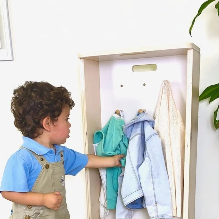 Boy child independently using the Sapiens Child Mango Montessori Cubby Coat Rack, demonstrating the child-height hooks and seat that support independent dressing and Montessori practical life routines