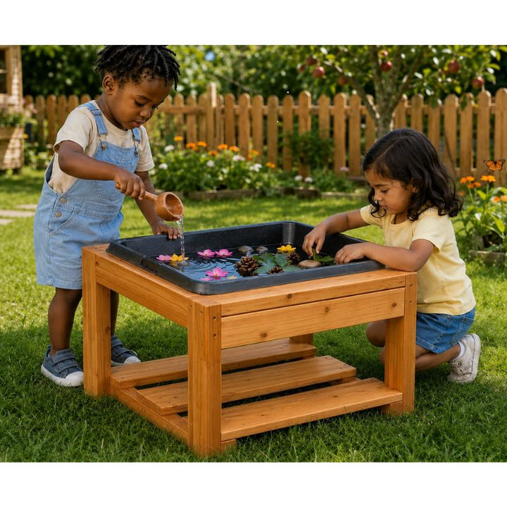 Two children playing at the ONP Mini Explorer Table outdoors, pouring water and floating flowers and pinecones in the built-in tray