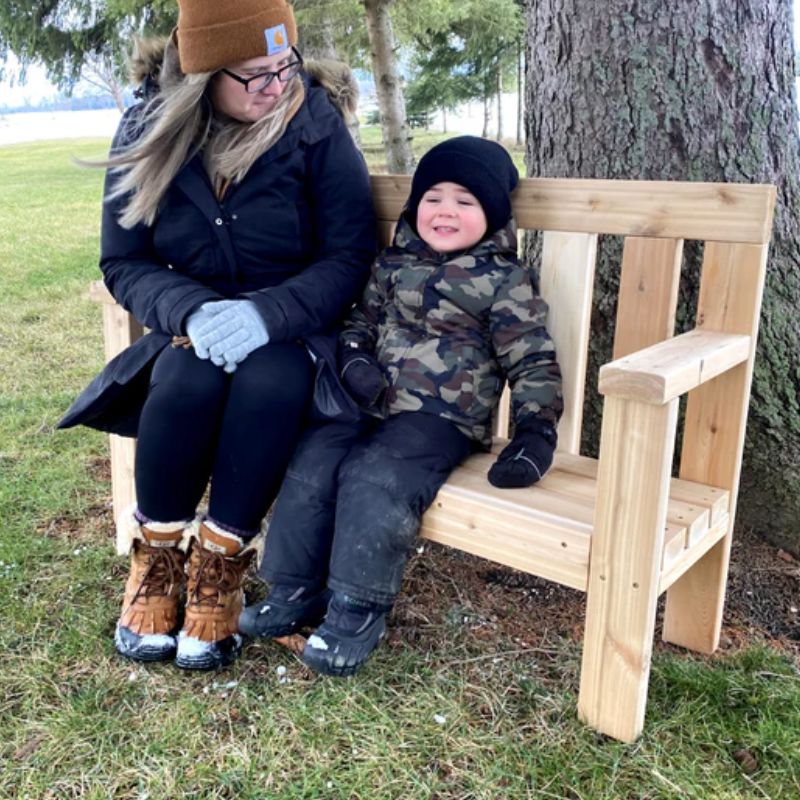 Adult and child sitting together on the ONP Preschool Buddy Bench, showing the cedar outdoor inclusion bench's taller armrests and 11-inch preschool seat height designed for both children aged 3 to 5 and adults