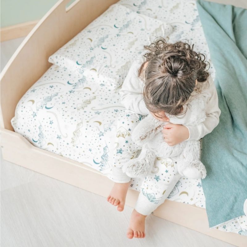 Child sitting on the Sapiens Child Cherry Twin Montessori floor bed, showing the low-profile design that supports toddler and kid independence at floor level