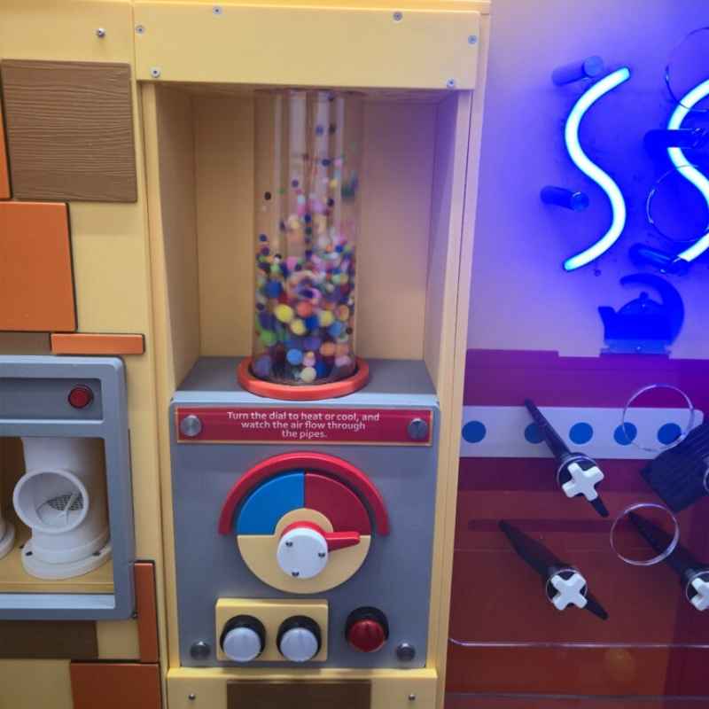 LiteZilla PomPom Cyclone sensory air tube mounted on a wall beside interactive lighting, with a dial that controls airflow through the tube