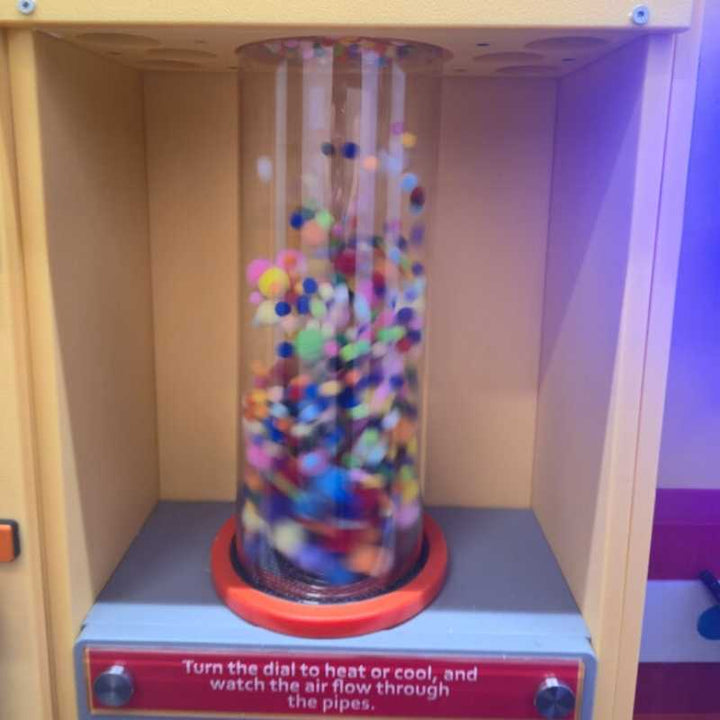 Colourful pom poms swirling in motion inside the LiteZilla PomPom Cyclone sensory air tube, capturing the dynamic visual effect in action