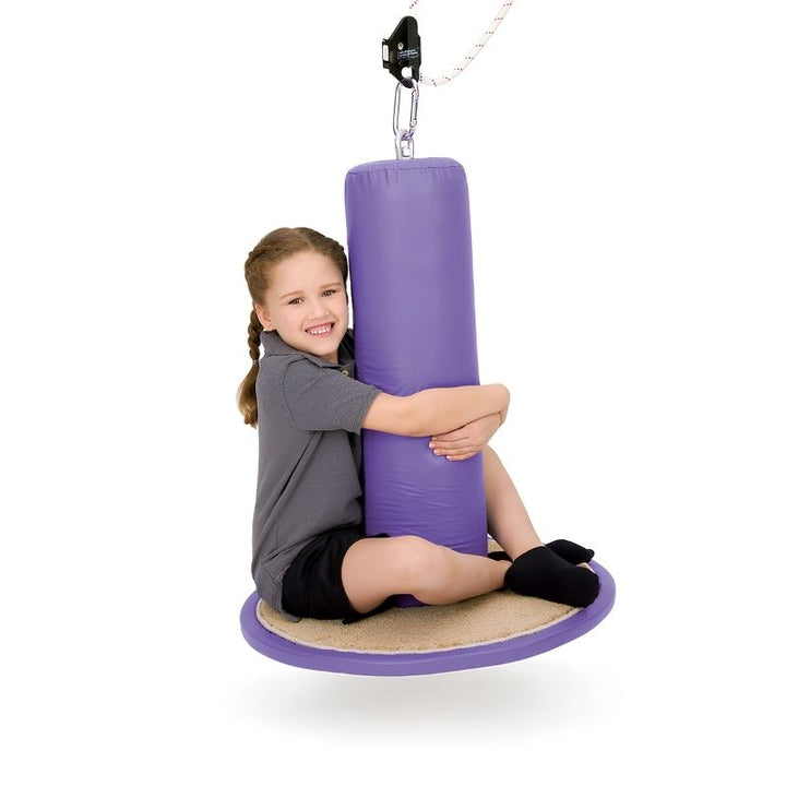 Child sitting on the Southpaw Flexion Disc Swing, actively engaging with the carpeted disc and centre post during a vestibular and proprioceptive therapy session