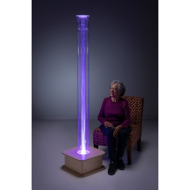 Elderly woman smiling in front of the Southpaw MSE+ Interactive Popcorn Tube 72", showing the sensory column supporting engagement and calm for adults in care settings