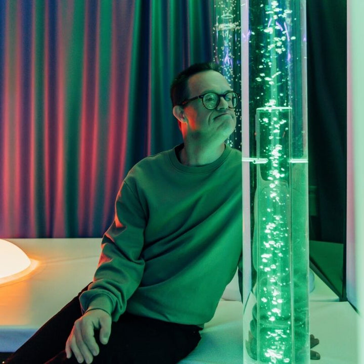 Adult interacting with TFH Aquarium Bubble Tube 6" showing the soothing LED colour-changing bubble column for dementia care, relaxation and anxiety de-escalation