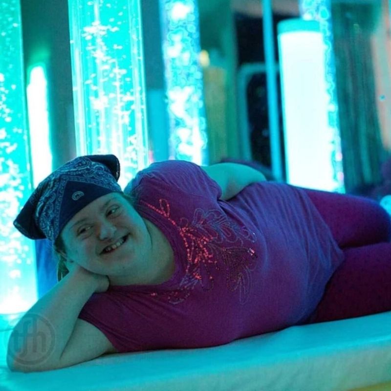 Child lying down happily beside TFH Aquarium Bubble Tube 6" showing the calming and relaxation effect of the rising bubble column for sensory regulation