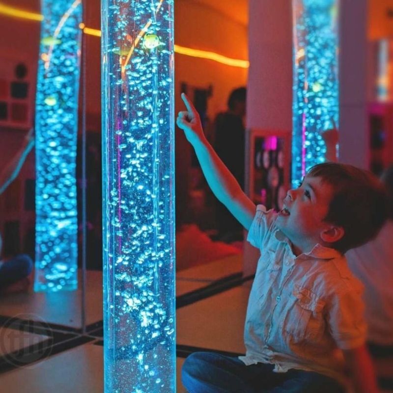 Child pointing upward at TFH Aquarium Bubble Tube 6" demonstrating visual tracking engagement with rising bubbles and colour-changing LED light in a sensory room