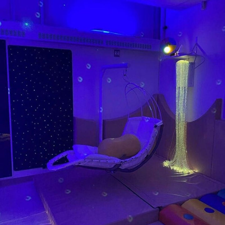 TFH Swaying Banana Leaf Chair in a blue-lit sensory room demonstrating the calming vestibular swing as part of a multi-sensory therapy environment