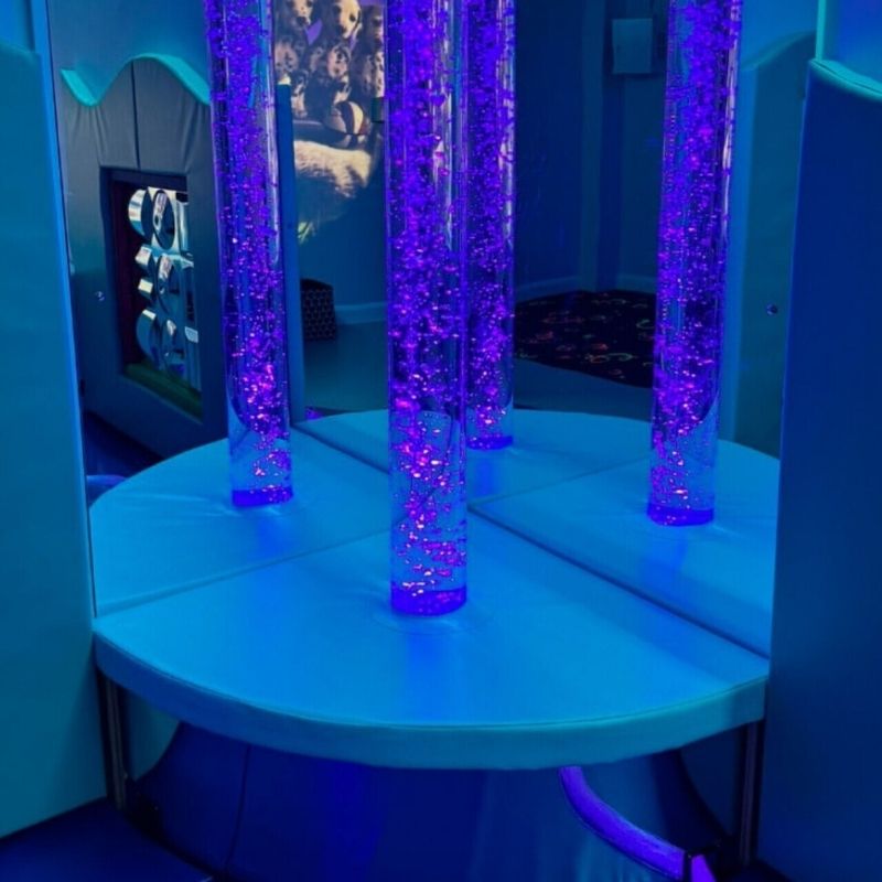 TFH Interactive Bubble Tube Corner Bundle installed in a sensory room corner showing the 80-inch bubble tube in blue light with corner podium, acrylic mirrors and wireless colour controller as a complete sensory corner kit